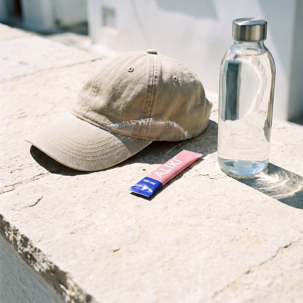 Faded cap with a dried salt line, an ALIKI stick and a clear bottle of water on pale limestone