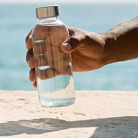 A hand lifts the capped bottle of clear drink off the ledge