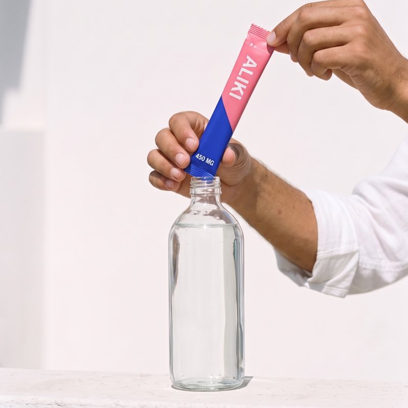 Hands tear an ALIKI stick at the notch over a clear bottle of cold water