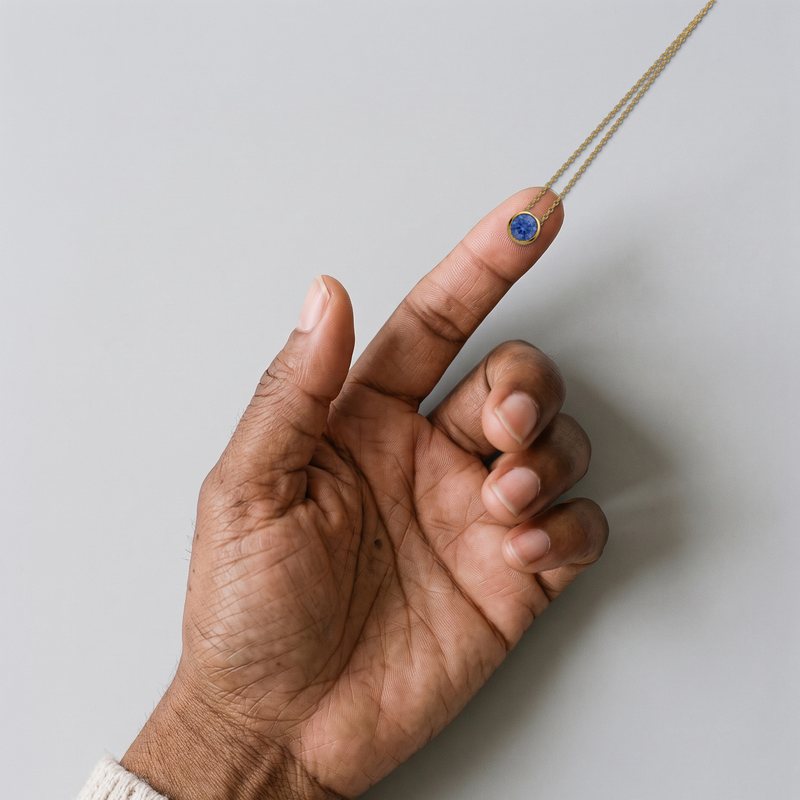 The Corund pendant on a fingertip: a 6.5 mm laboratory-grown sapphire in an 8.3 mm bezel