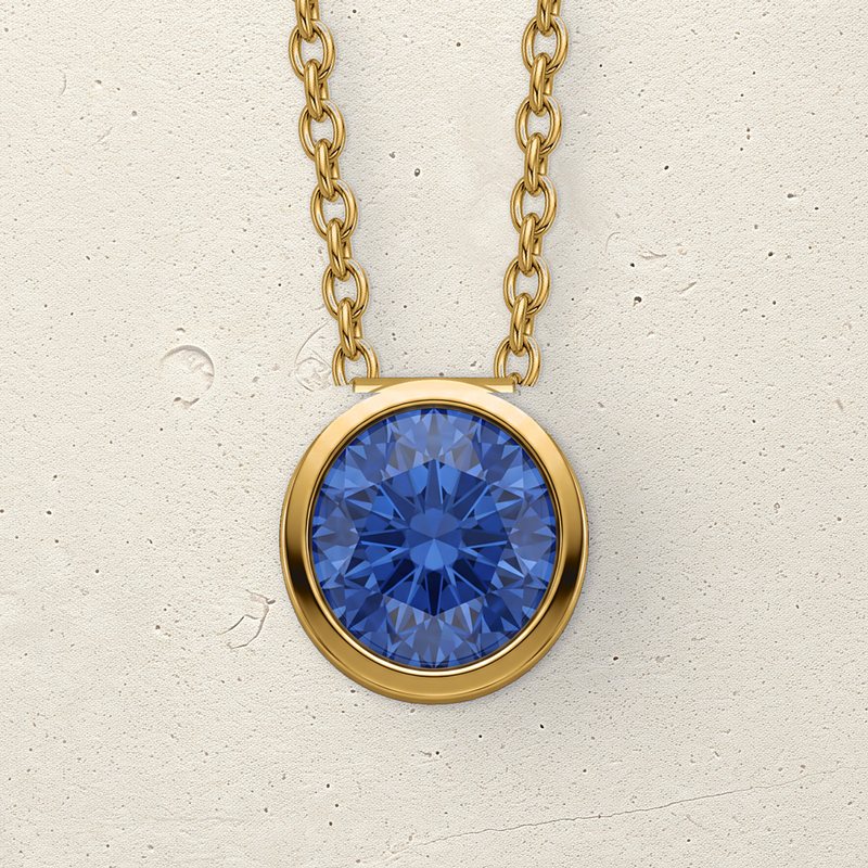 The Corund vermeil pendant with its laboratory-grown blue sapphire lying on pale limestone