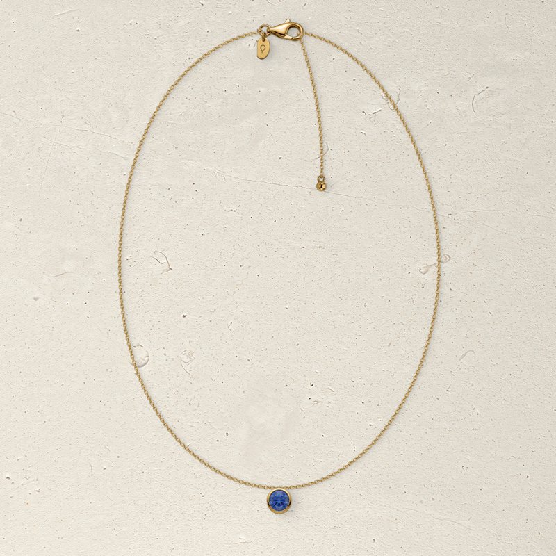 The whole Corund necklace laid in an oval on pale limestone: chain, clasp, tag and pendant