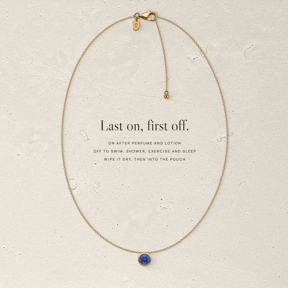 Corund vermeil necklace laid flat on pale limestone, with three care steps