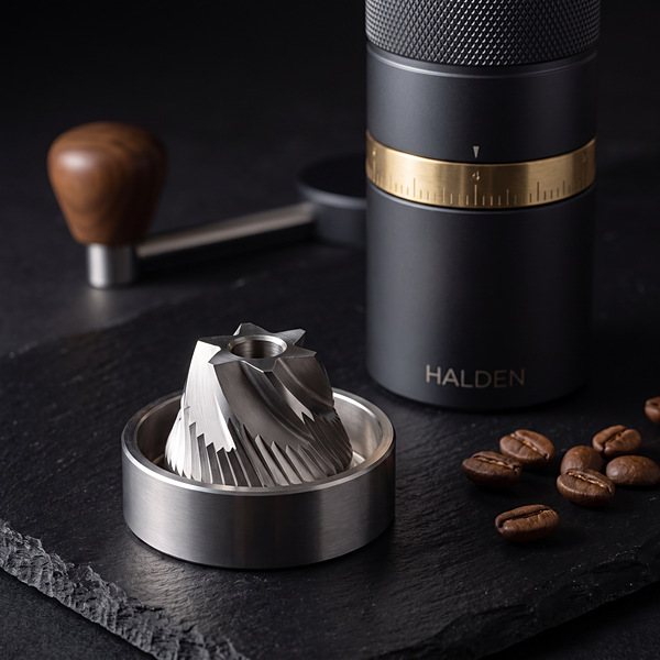Conical stainless steel burr set of the Halden One standing on black slate beside whole beans