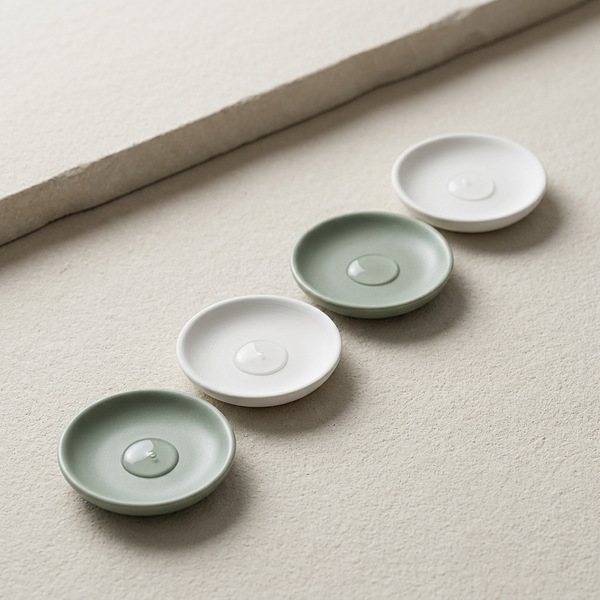 Four celadon lab dishes with a clear drop each, on pale limestone in late side light