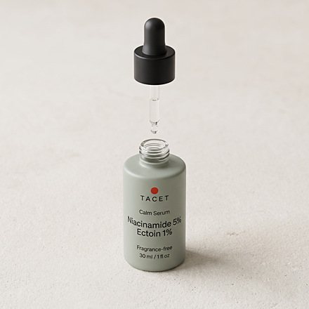 Open Tacet bottle on pale stone beside folded oat linen, dropper seated in the neck, from above