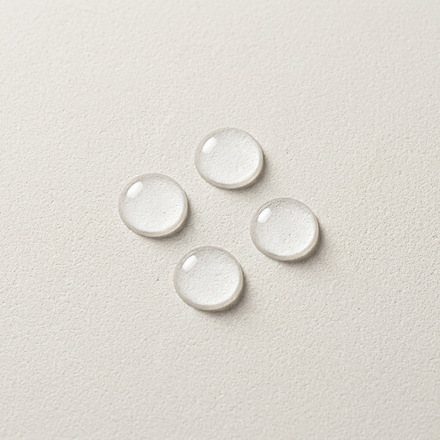 Four clear serum drops resting on a pale stone surface in soft daylight