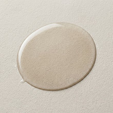 A thin spread film of clear serum on pale stone in soft daylight