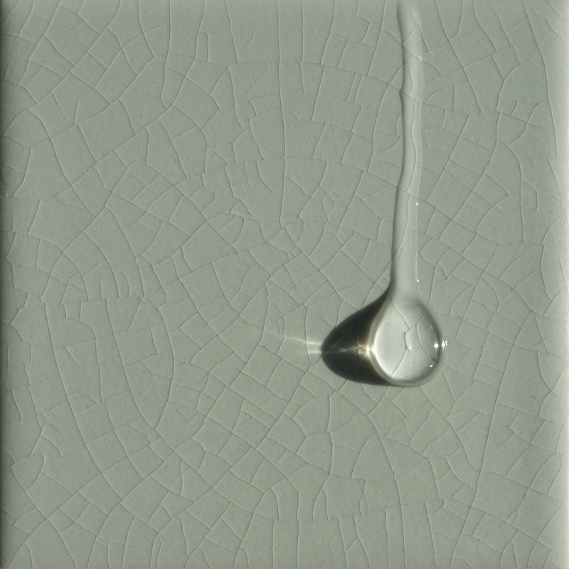 One clear drop of serum sliding down a crackle-glaze celadon tile